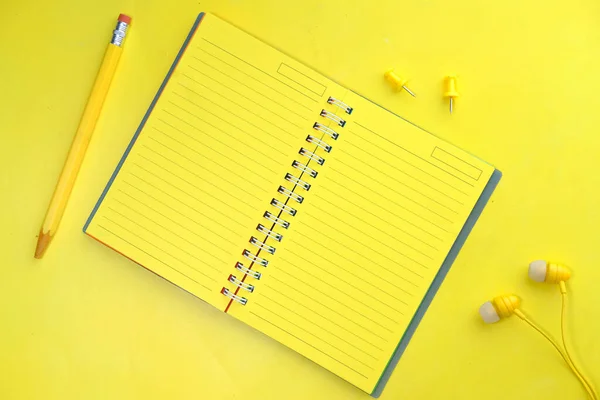 Notebook, lápis e fone de ouvido em fundo amarelo — Fotografia de Stock