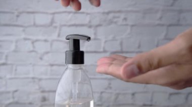 Virüsü önlemek için el dezenfektanı kullanan sıradan giysili genç bir adam. 