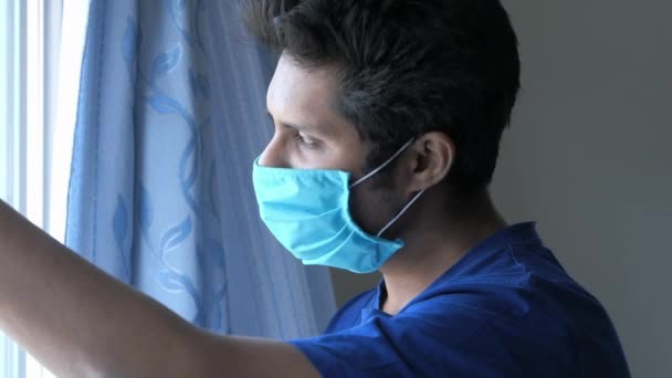 Un hombre enfermo con una máscara en la cara mirando por la ventana — Vídeo de stock