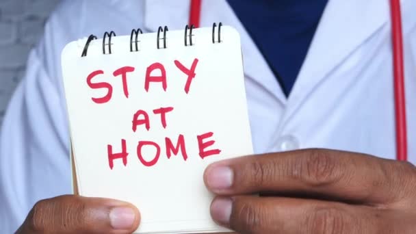 Χέρια του γιατρού κρατήστε ένα σημειωματάριο με τις λέξεις μείνετε στο σπίτι. — Αρχείο Βίντεο
