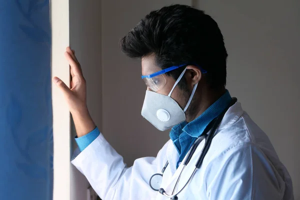 Γιατρός φορώντας μάσκα προστασίας προσώπου κοιτάζοντας μέσα από το παράθυρο — Φωτογραφία Αρχείου
