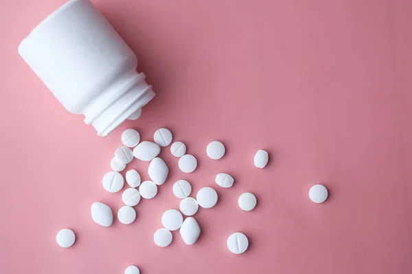 bottle of white pills on pink background