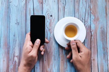 Elleri boş ekranlı cep telefonu ve kahve fincanı tutan bir adam..