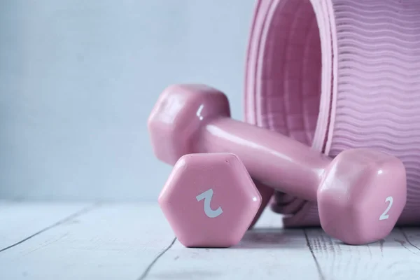 Закрыть гантели розового цвета и коврик для упражнений на столе — стоковое фото