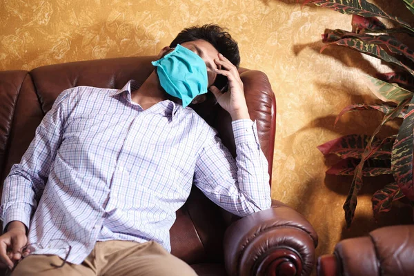 Ένας άρρωστος με μάσκα στο πρόσωπό του να αναπαύεται στον καναπέ. — Φωτογραφία Αρχείου