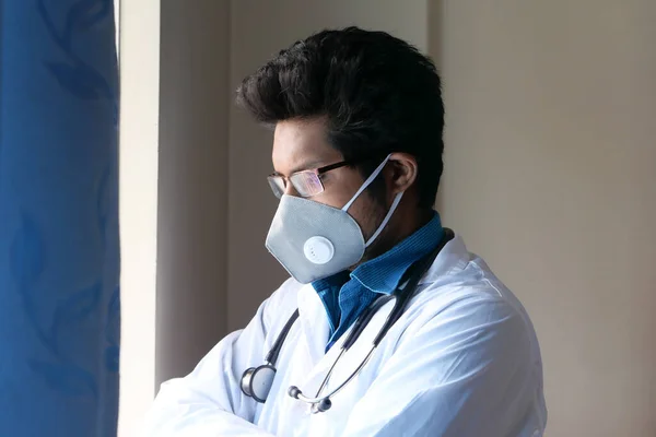 Dokter met gezichtsmasker kijkend door het raam — Stockfoto
