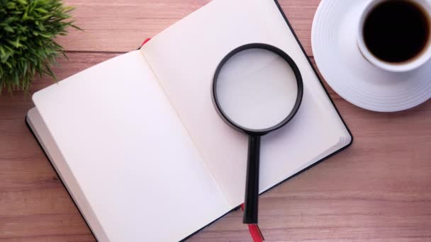 Open book and magnifying glass on table. — Stock Video