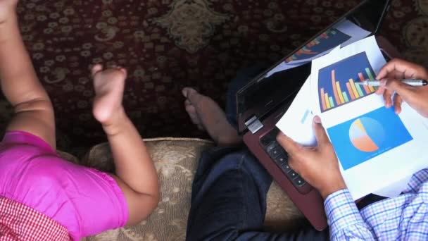 Концепция работы из дома, молодой человек анализирует графики и детская игра на полу — стоковое видео