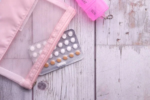 birth control pills and pill box on wooden table