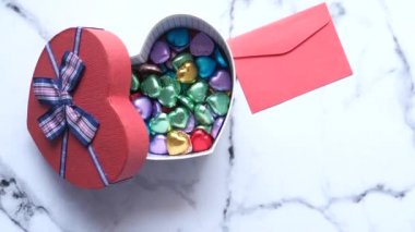 Kalp şeklinde bir hediye kutusundaki şekerin en üst görüntüsü. Masada zarf var..