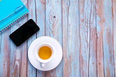 Boş ekran ve tahta arkaplanda not defteri olan akıllı telefonun üst görünümü 