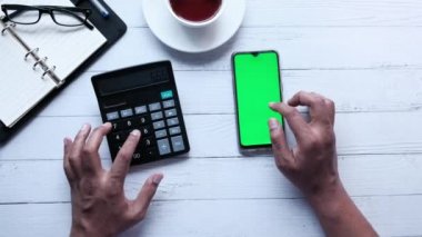 Yeşil ekranlı akıllı telefon kullanan ve hesap makinesine güvenen kişi 