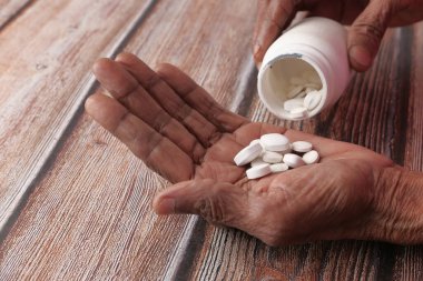 Yaşlı kadın elinde fotokopi aletiyle şişeden ilaç dolduruyor. 