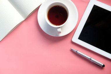 Pembe üzerine dijital tablet, çay ve not defterinin üst görünümü 