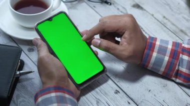 İş adamı eli masada yeşil ekranlı akıllı telefon kullanıyor. 