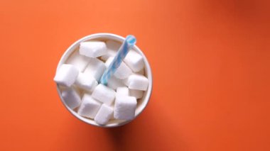 Turuncu zemin üzerinde plastik bir kabın içindeki şeker küpünün üst görünümü 