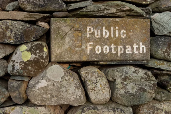 Stone Public Footpath Sign.  The stone public footpath sign is embedded in a dry stone wall and is situated alongside Ullswater lake in the English Lake District national park.