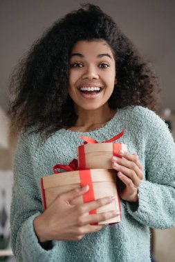 Güzel Afrikalı Amerikalı kadın hediye kutuları tutuyor, kameraya bakıyor ve gülümsüyor. Ellerinde doğum günü hediyeleriyle genç duygusal bir kızın portresi.
