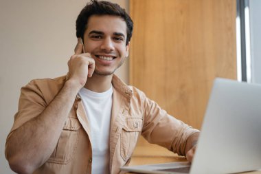 Yakışıklı Hintli adam cep telefonuyla konuşuyor, kameraya bakıyor ve gülümsüyor. Asyalı iş adamı işe başlıyor, dizüstü bilgisayar kullanıyor, akıllı telefon tutuyor, ofiste iletişim kuruyor. Başarılı bir iş. 