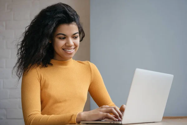 Beautiful African American woman using laptop computer, internet, watching training courses online. Businesswoman working in office, typing, searching on website. Happy successful student studying