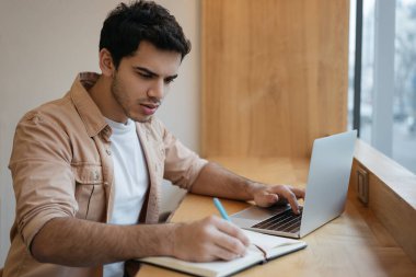 Modern ofiste çalışan dalgın Hintli işadamının portresi. Laptop kullanan, daktilo kullanan, not defterine not alan yakışıklı bir serbest çalışan. Üniversite öğrencisi, sınav hazırlığı