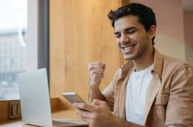 Genç, yakışıklı Hintli adam cep telefonu tutuyor, iletişim kuruyor, mesaj alıyor, iyi haberler okuyor. Asyalı iş adamı, mutlu duygusal yüz kutlama başarısı ile modern ofiste oturuyor. 