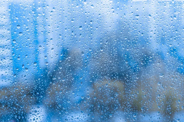 rain drops on the glass window. night rainy window in autumn spring summer. abstract natural view. rainy season. droplets on blue glass window shield.
