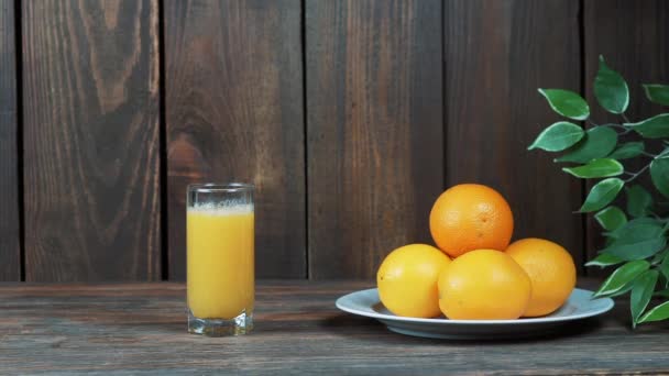 グラスの中で絞りたてのオレンジジュースが木の背景に絞りオレンジジュースを注ぐ — ストック動画