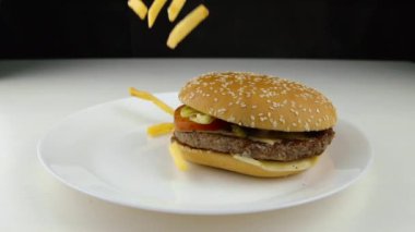 Hamburgerin üstüne kızarmış patates cipsi düşüyor ağır çekimde fast food abur cubur konsepti 
