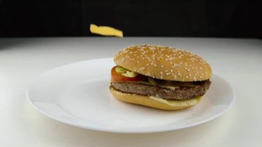 Hamburgerin üstüne kızarmış patates cipsi düşüyor ağır çekimde fast food abur cubur konsepti 