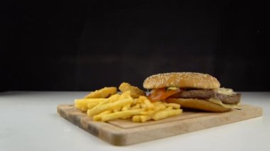 Siyah bir zemin üzerinde havada yüzen malzemelerle dolu bir hamburger.