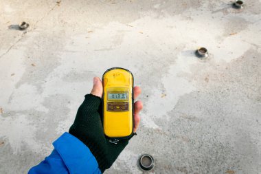 Person hands holding yellow gadget  with screen- dosimeter\geiger counter .Memorial of Chernobyl.  On screen minimal radiation level shown.2019.10.08.