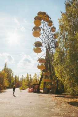 Unused ferris wheel in abandoned SSRS town Pripyat from1970s with one tourist. Vertical photo with a sunflare in the background and autum nature around.2019.10.08