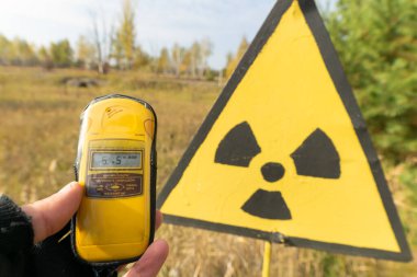 Yellowgeiger counter on the hands shows radiation level near radiation symbol in front of red forest in autumn.Ukraine. Chernobyl group tour.