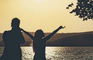 Annenin göl kenarında manzaralı bir yerde kızının fotoğrafını çekerken çekilmiş panoramik bir fotoğrafı. İki kişinin silueti.