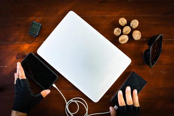 Many portable gadgets on the red wooden table pushed with hands.Charging set up while travelling light. Energy for personal portable electronic items.