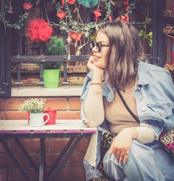 Vintage image of beautiful female person wth glasses who is sitting in a cafe and looking to her right side.. Retro style background image with hearts hanging in the background.