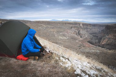 Mavili erkek çadırın yanında oturur ve düşünürken ve Ihlara vadisine bakarken kahve içer. Türkiye 'de doğa kampı.