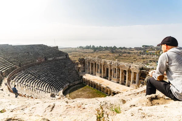 Wide Panorama of ancient  greek amphitheatre in Hierapolis with the person sitting on the right. Tourists attractions and historical landmarks in Turkey. 2019.11.27.