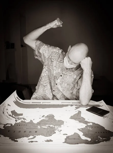 Black and white image of Angry tourist male person in the room with clutched fist hits the world map with passport on the side. Concept of ruined travel plans due to pandemic and corona virus and flights cancelation.