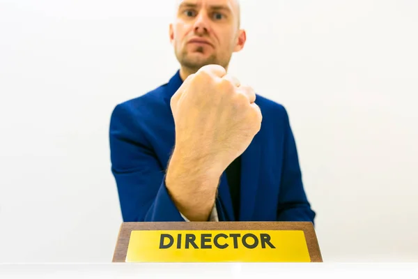 身穿蓝色西服的愤怒的男老板正举着拳头 面前摆放着一个商业职位牌 — 图库照片
