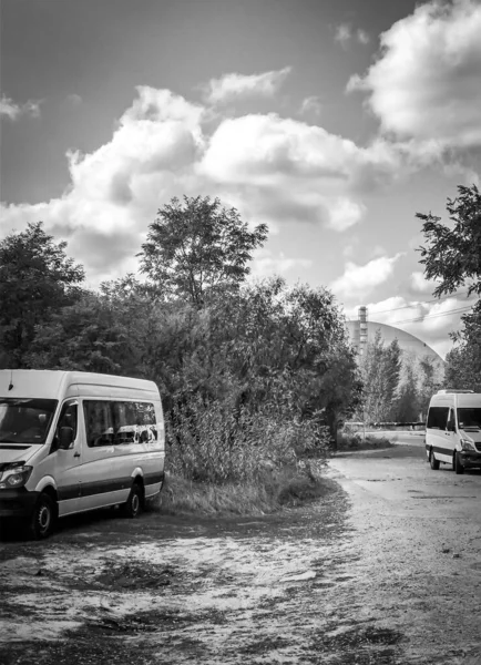 Two mini muses are standing on the road parked with chernoby black 4 reactor on the background. Tours and excursions in  Ukraine. Black and white background image.2020