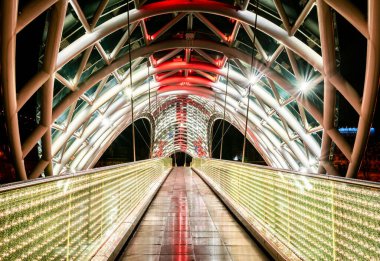 Tblisi 'de gece vakti mimarinin panoramik görüntüsü ve iliuminated Peace Köprüsü' nün yolu. Georgia.25.03.2020.