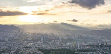 Uzak mesafeden Tiflis şehir binalarına dramatik hava manzaralı arka planda kafkas dağları ve günbatımını gösteren 2020.