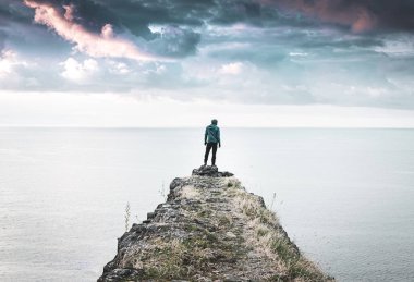 Günlük kıyafetli bir adam tarihi yapının kenarında duruyor ve arkasında deniz ve dramatik gökyüzü olan sağa bakıyor. Huysuz, boş uzay görüntüsü. 2020