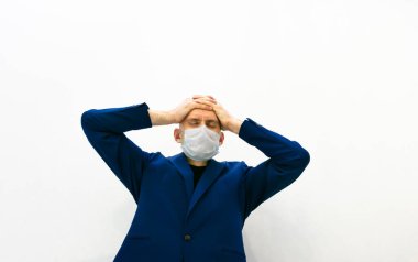 Mavi ceketli ve beyaz arka planda tıbbi maskeli biri hayal kırıklığını gösteriyor ve kafasını ellerle örtüyor. Corona virüsü salgını yüzünden işteki umutsuzluk ve hüsran.
