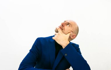 Mavi ceketli bir iş adamı avucunu yanağında tutar ve düşünürken kafasını kaldırır. Boş uzay görüntüsü. Karar verme yüz konsepti.