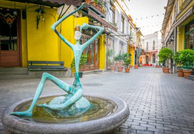 Yüzünde cerrahi maske olan bir heykel ve turistler olmadan boş bir patika. Kapalı kafeler ve restoranlar. Tiflis 'teki karantina sırasında turizm sektörü konsepti. Avrupa. 20.04.2020