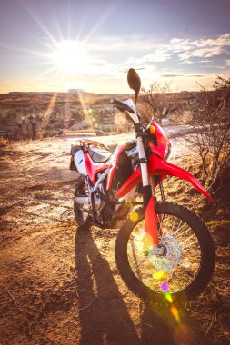 Kapadokya 'nın Goreme kasabasının önünde güneş doğarken kırmızı serin çapraz yarış motosikleti duruyor. Arka plan dikey fotoğrafı. 2019.12.15.