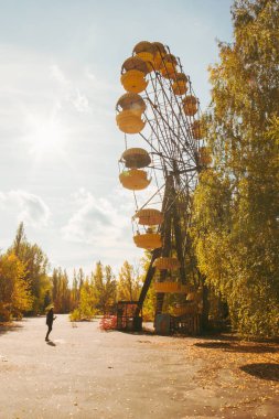 Unused ferris wheel in abandoned SSRS town Pripyat from1970s with one tourist. Vertical photo with a sunflare in the background and autum nature around.2019.10.08